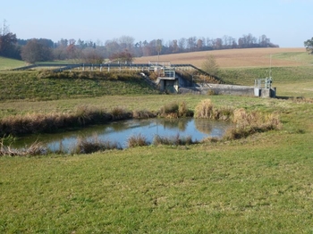 Ansicht auf Erddamm und Durchlassbauwerk vom Beckeneinstauraum